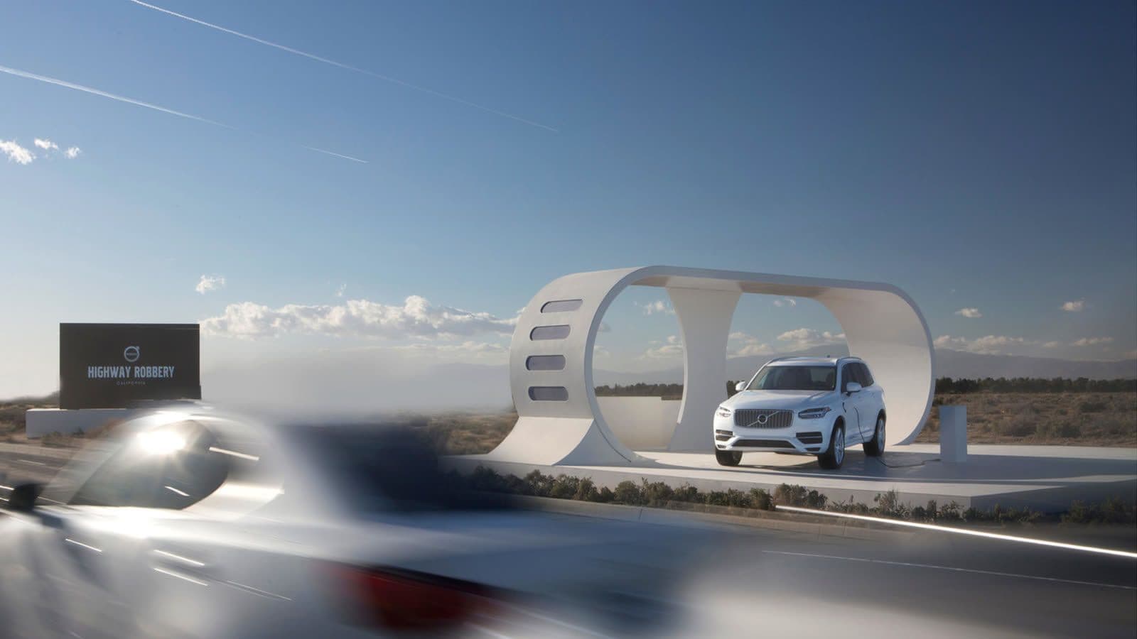 Volvo XC90 displayed beside the Highway Robbery kinetic charging installation as cars pass on a California highway.